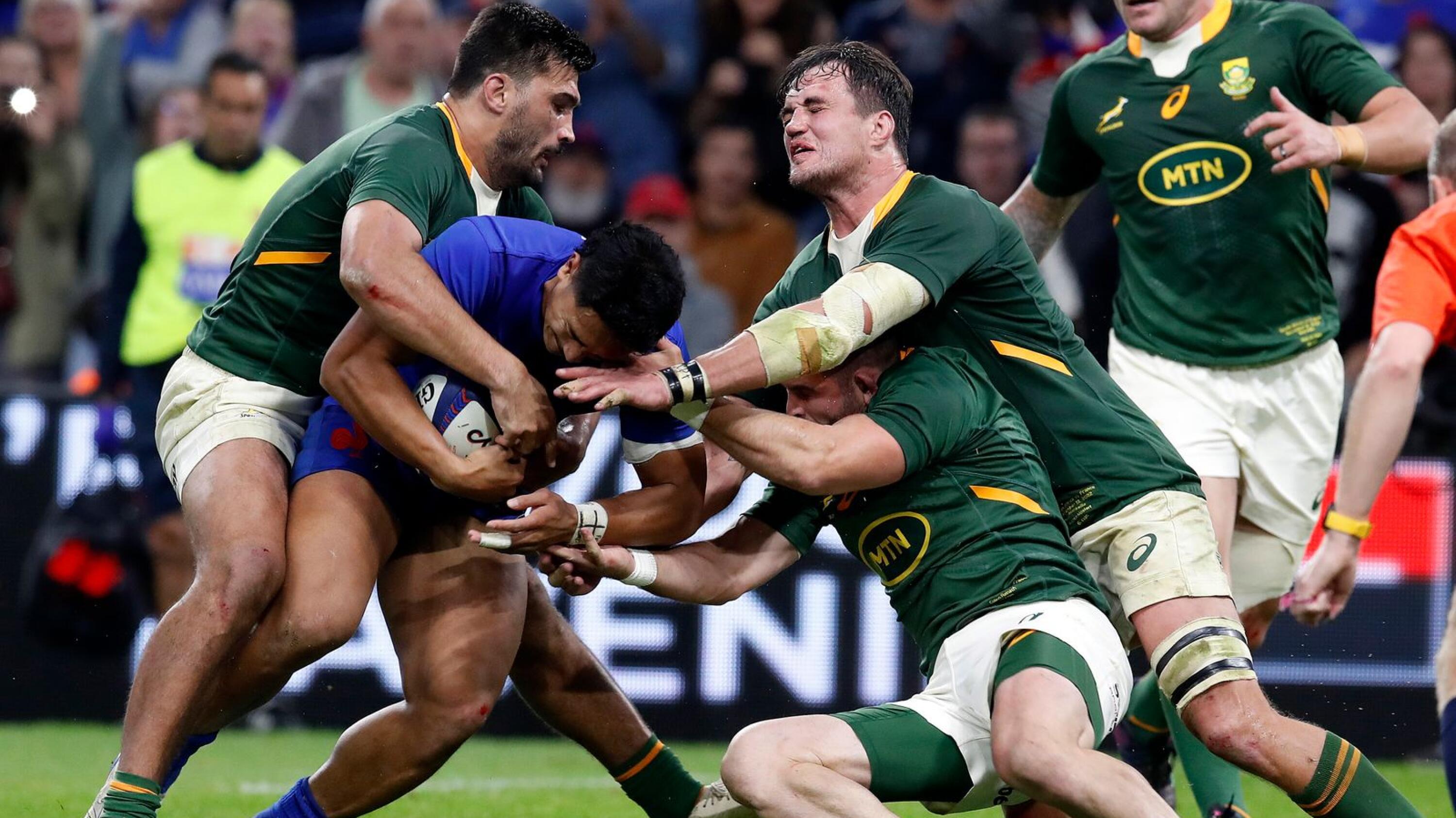 Springbok rugby players in green attempt to tackle a French rugby player in blue with the ball