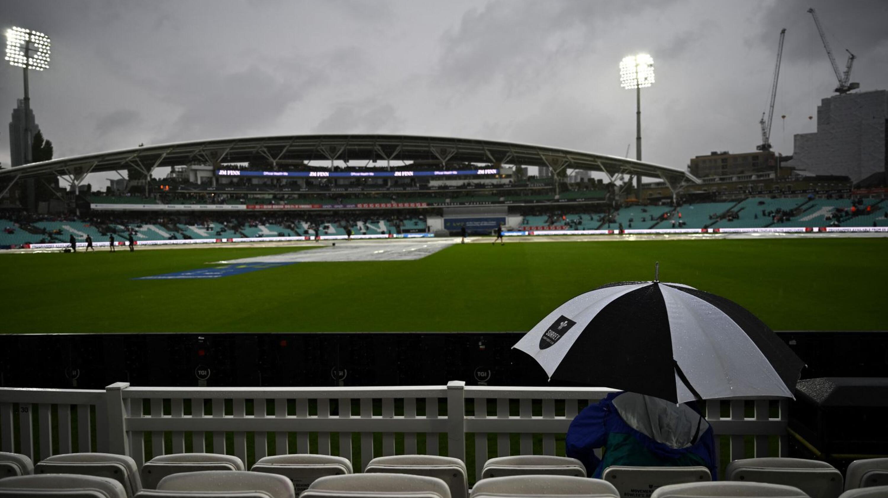 A fan sits under an umbrella as the rain falls down while they game didn't start yet due to the weather condition on day 1 of the third Test match between England and South Africa at the Oval in London on Thursday