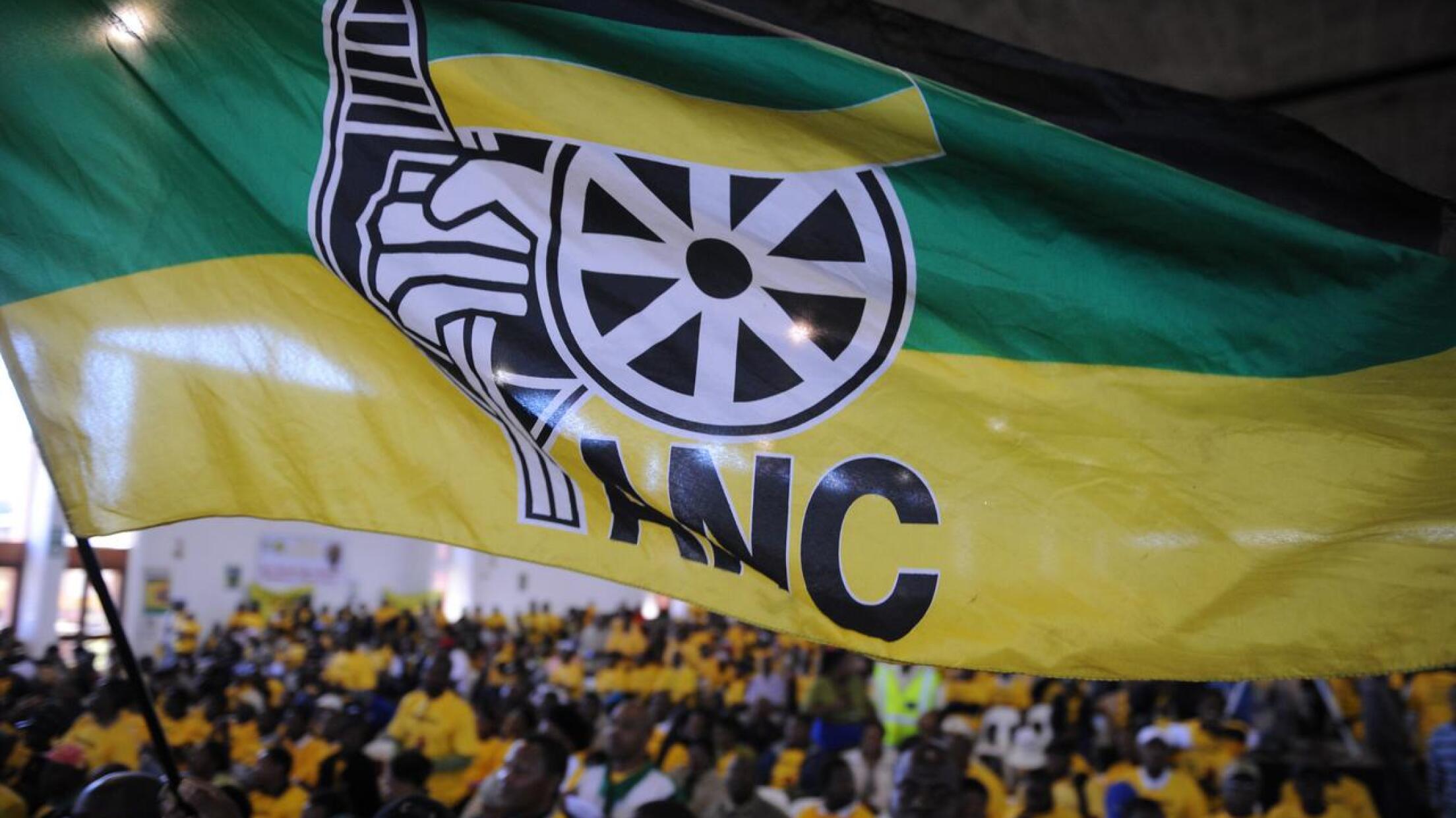 A flag flies above ANC members at a meeting. 