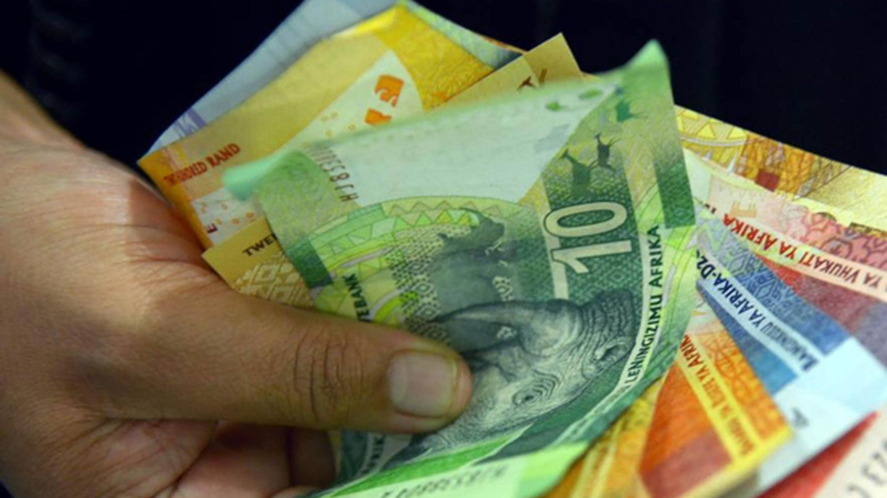 A hand holding South African bank notes.