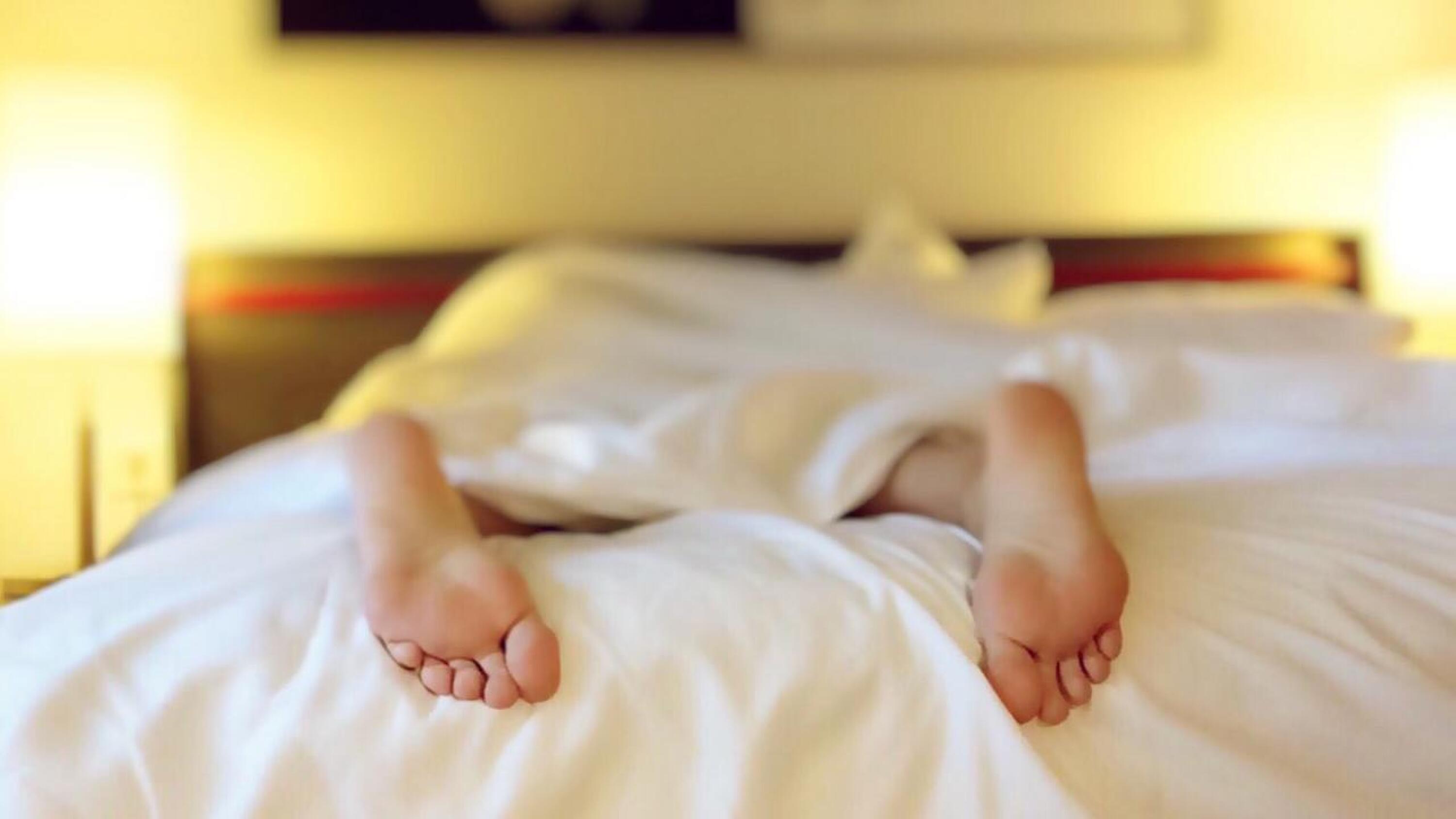 Picture of naked feet protruding from the sheets of a rumpled bed.