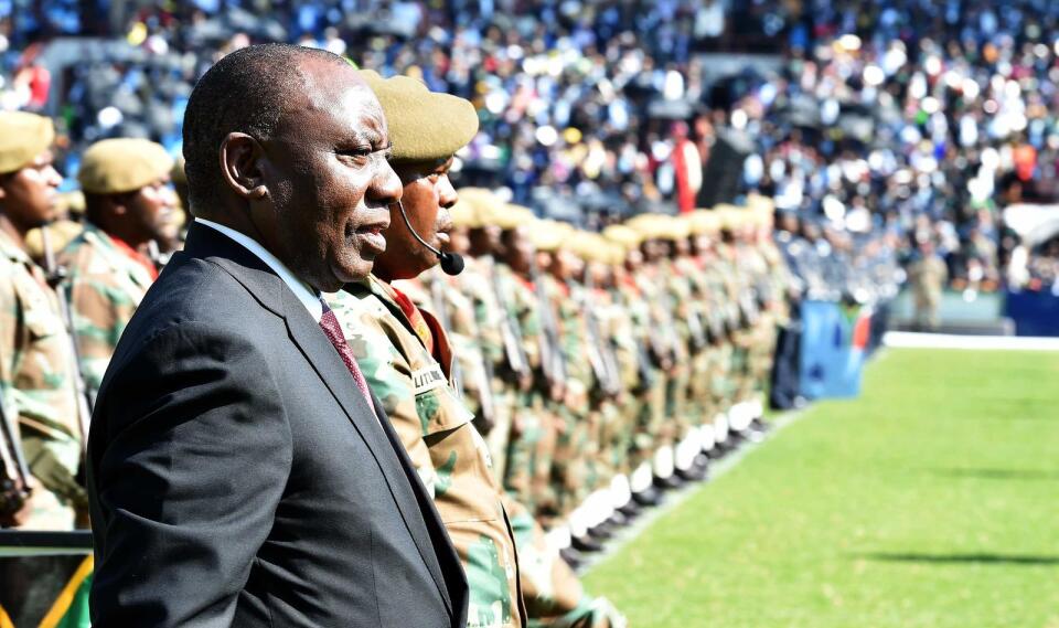 South African President Cyril Ramaphosa stands in a stadium at the end of a long row of soldiers.
