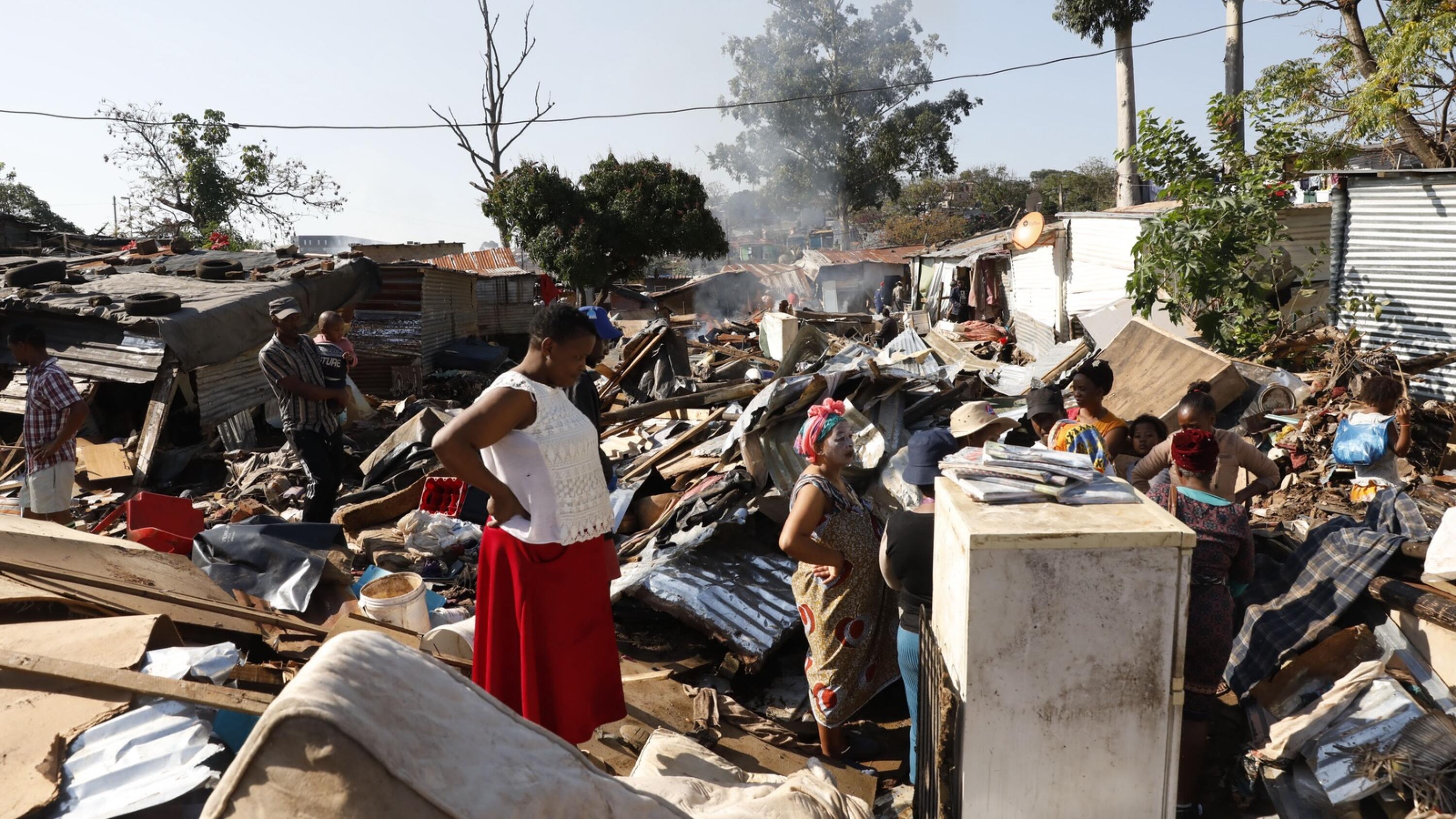Women stand among debris including beds and roof sheets.