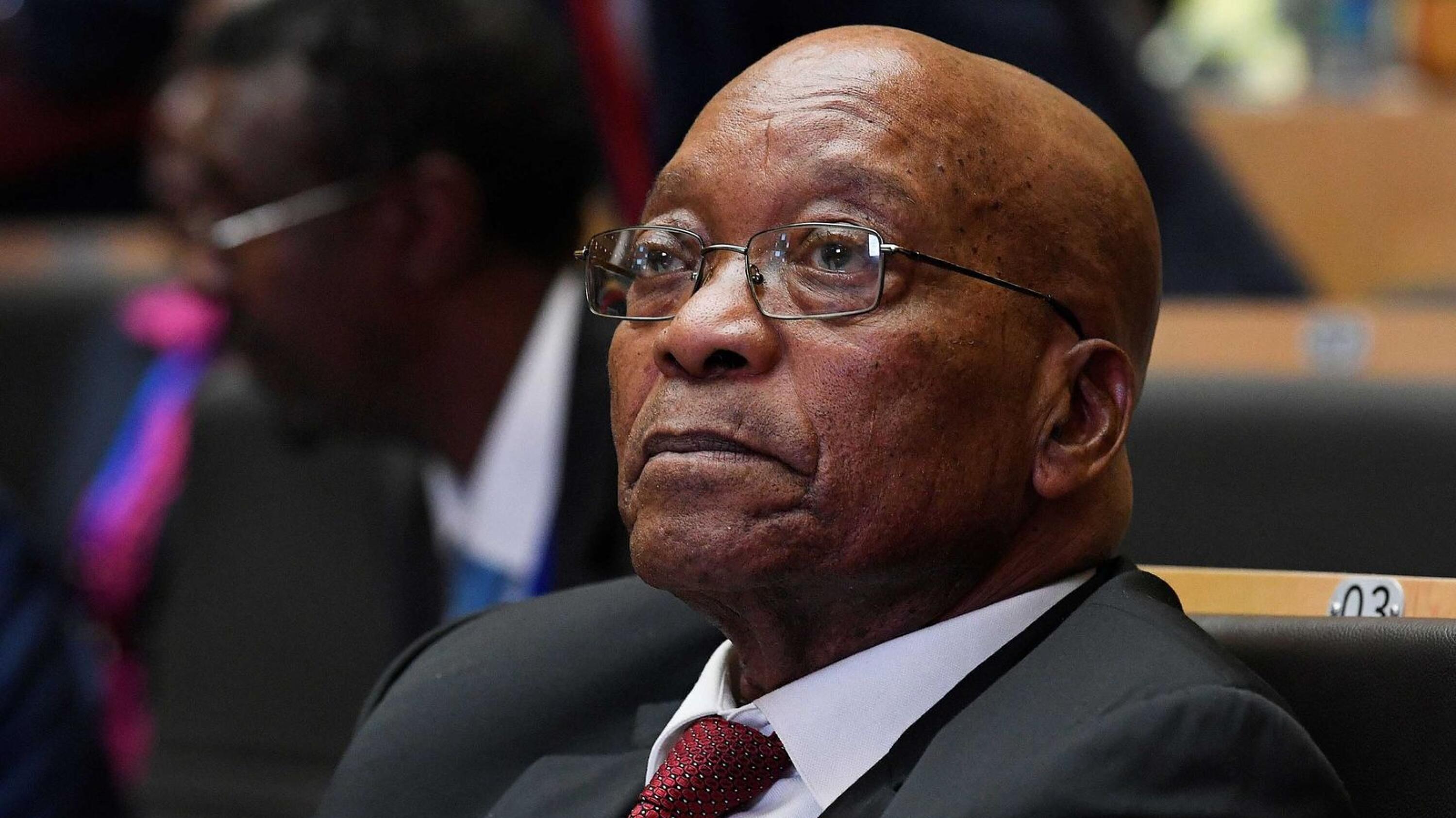 Zuma dressed in a suit seated at a table.