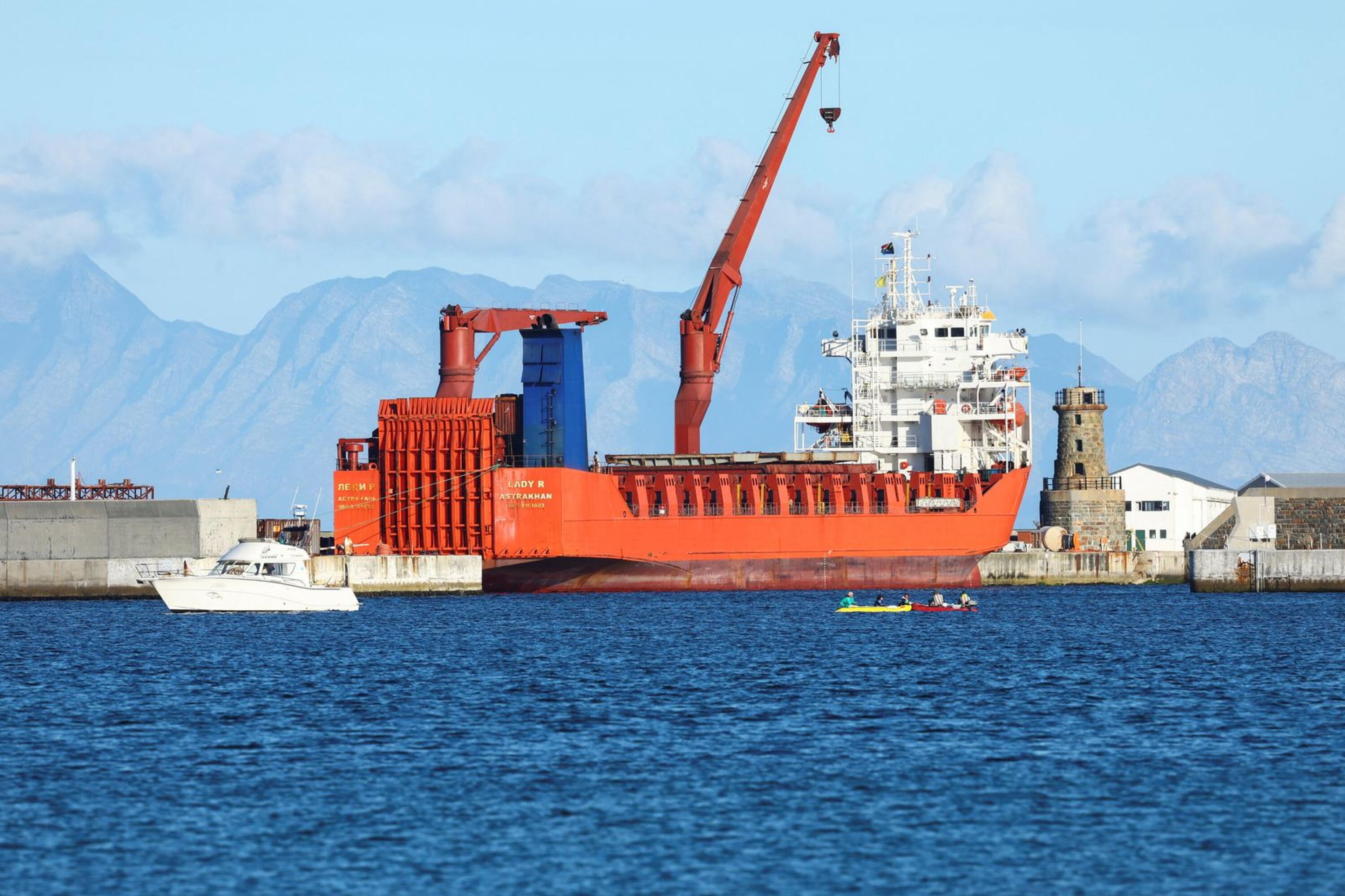 A large red ship is seen with buildings behind it.