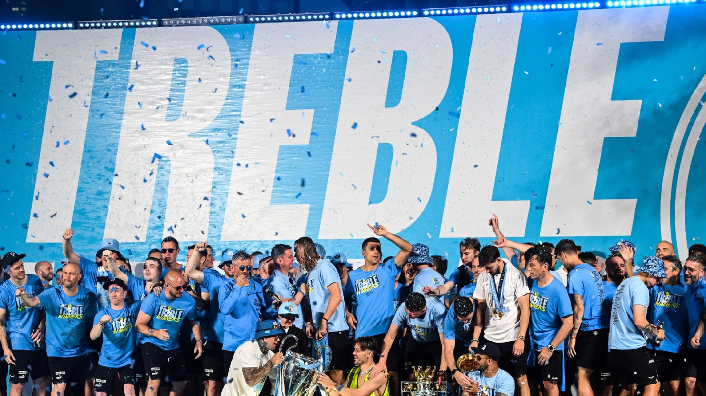 Manchester City's players celebrate on stage with their trophies following an open-top bus victory parade for their Champions League, FA Cup and Premier League victories. 
